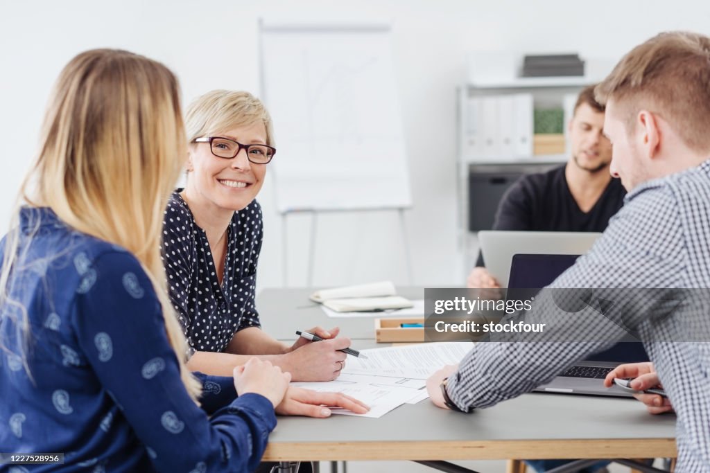 Smiling woman in a meeting with business co-workers as they sit grouped around a table discussing paperwork